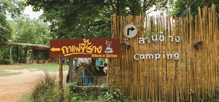 ป้าย "ค่ายไทย" ตั้งอยู่หน้ากำแพงไม้ไผ่ สื่อถึงการตั้งแคมป์ในบรรยากาศที่เป็นธรรมชาติ