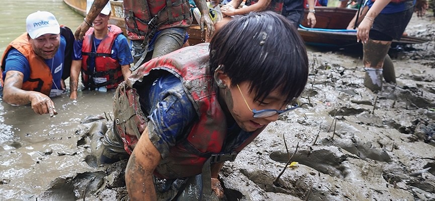 เด็กชายในเสื้อชูชีพกำลังคลานผ่านโคลนอย่างตั้งใจและมุ่งมั่นในกิจกรรมกลางแจ้ง