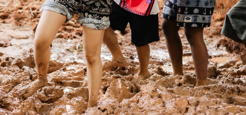 กลุ่มวัยรุ่นสามคนยืนอยู่ในโคลน สื่อถึงความสนุกสนานและการผจญภัยในธรรมชาติ