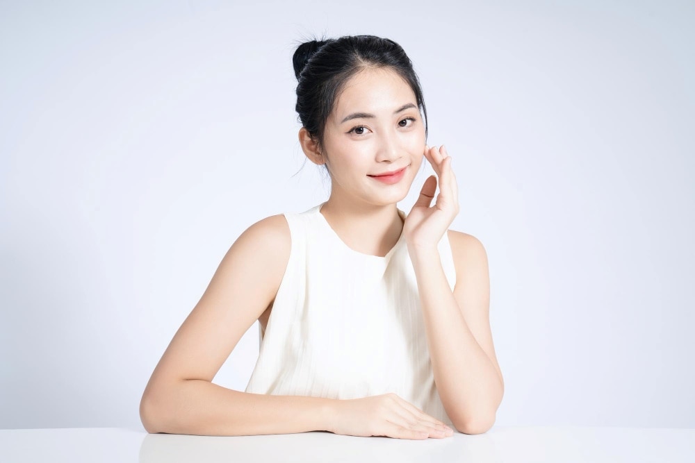 หญิงที่นั่งอยู่ที่โต๊ะสวมเสื้อแขนกุดสีขาว เผยให้เห็นถึงผิวพรรณที่สวยงาม